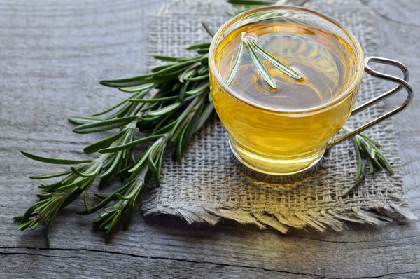چای گیاهی رزماری در یک فنجان شیشه ای بر روی زمینه چوبی روستایی چای رزماریتمرکز انتخابی