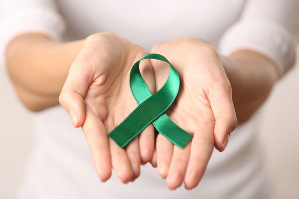 نمای نزدیک دست زنان که روبان سبز دارند بیماری میتوکندری و مفهوم سرطان کلیه