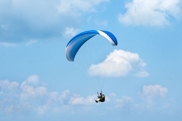 پاراگلایدر آبی در پس زمینه ابرها در آسمان آبی پرواز می کند پاراگلایدر در آسمان در یک روز آفتابی