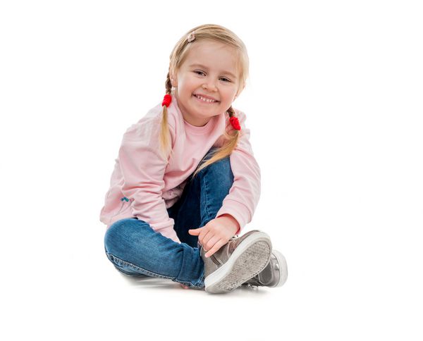 دختر کوچولوی دوست داشتنی که روی زمین نشسته است روی زمینه سفید جدا شده است