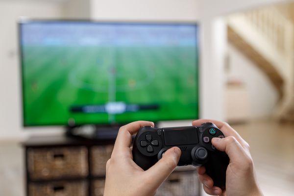 بازی ویدیویی مرد دست کنترلر کنسول فوتبال یا بازی فوتبال در تلویزیون تلویزیون عریض صفحه نمایش روی کالا قرار دارد