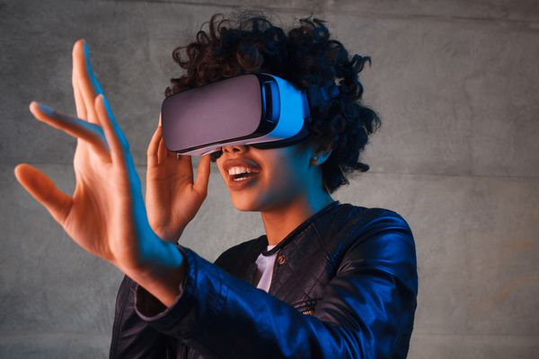 زن جوان شگفت زده که هنگام تجربه VR با هوا تماس می گیرد شات استودیوی افقی