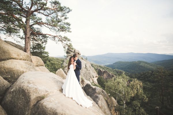 عروس زرق و برق دار بوسیدن داماد و بغل کردن در نزدیکی صخره ها با نمای خیره کننده