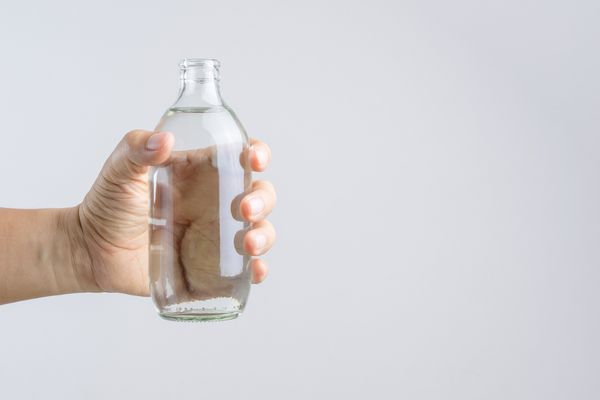 بطری آب شیشه ای با دست را در زمینه سفید نگه دارید