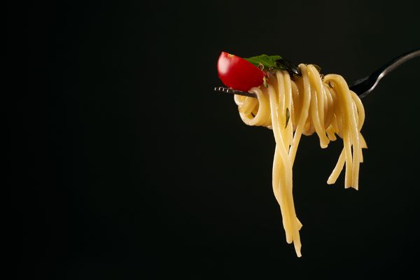 اسپاگتی روی چنگال اسپاگتی با گوجه فرنگی گیلاس و ریحان تازه جدا شده در زمینه سیاه و با فضای کپی مفهوم غذای سالم و گیاهی