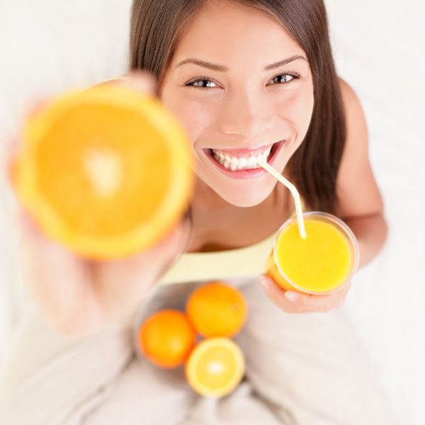 زن در حال نوشیدن آب پرتقال که لبخند خود را نشان می دهد مدل زیبا و نژاد مخلوط نژاد آسیایی قفقازی