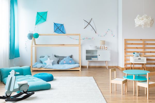 اسباب بازی سنگی مدرن و تشک آبی روی فرش سفید در اتاق خواب بچه ها با مبلمان دستباف