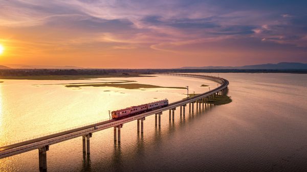 نمای هوایی این قطار روی پل بالای رودخانه سا سا سد لوپبوری تایلند و غروب آفتاب زیبا در حال حرکت است
