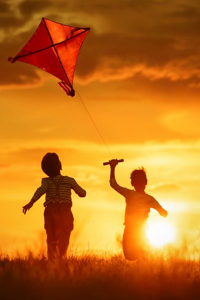 کودکان هنگام غروب آفتاب یک بادبادک را در این زمینه پرتاب می کنند