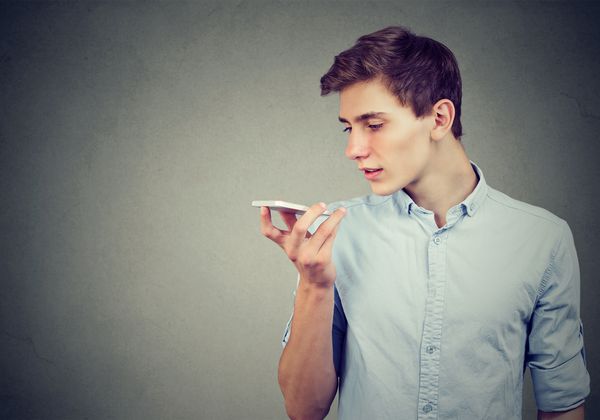 مرد جوان با استفاده از یک عملکرد تشخیص صدای تلفن هوشمند جدا شده در پس زمینه دیوار خاکستری