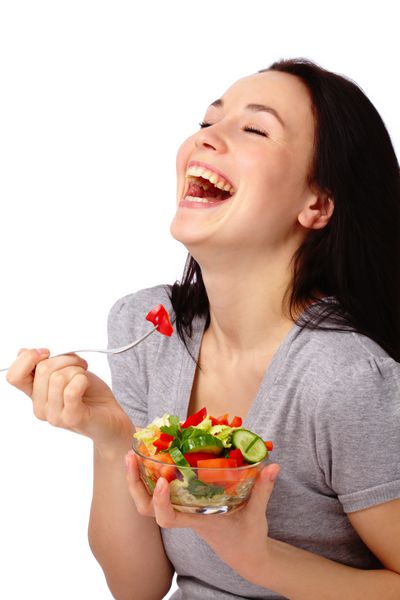 زن جذاب جوان سالاد سبزیجات را با استفاده از چنگال جدا شده از رنگ سفید می خورد
