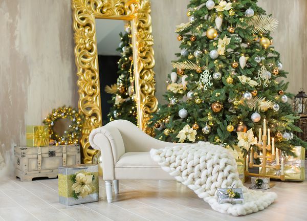 تزیینات استودیوی طلای کریسمس کریسمس با دختر ناز و آینه ای عظیم با قاب های طلایی و شمع های بزرگ و درخت کاج سبز بزرگ