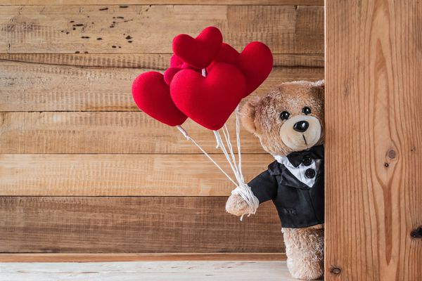 عکسی از خرس عروسکی ناز که دارای بادکنک قلبی شکل با بافت تخته چوب است