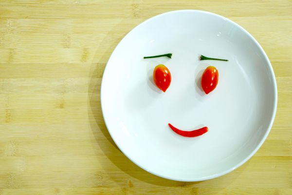 پوست گوجه فرنگی و فلفل دلمه ای لبخند را روی صفحه سفید می پوشانید دو گوجه فرنگی برای چشم و فلفل تند برای دهان احساسات لبخند از سبزیجات ساخته شده است مفهوم هنر غذا سبزی را دوست دارم فضای خالی