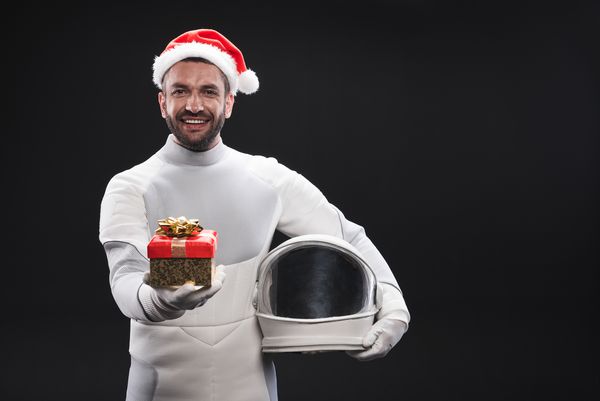 این مال تو است فضانورد جوان مبارک و با لباس سفید و کلاه سانتا قرمز در حالی که جعبه را با هدیه کریسمس در دست دارد با کلاه ایستاده است با فضای کپی جدا شده