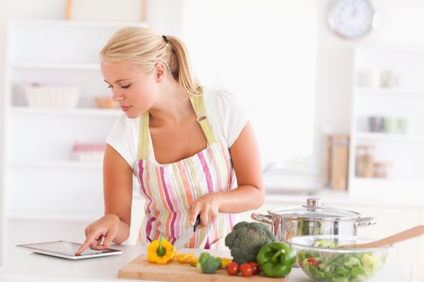 زنی که از رایانه لوحی برای پخت و پز در آشپزخانه خود استفاده می کند