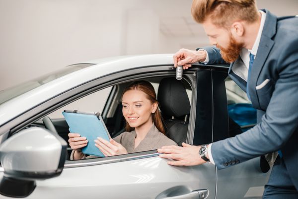 فروشنده ریشو دادن کلید ماشین به زن جوانی که در اتومبیل جدید با تبلت دیجیتالی نشسته است