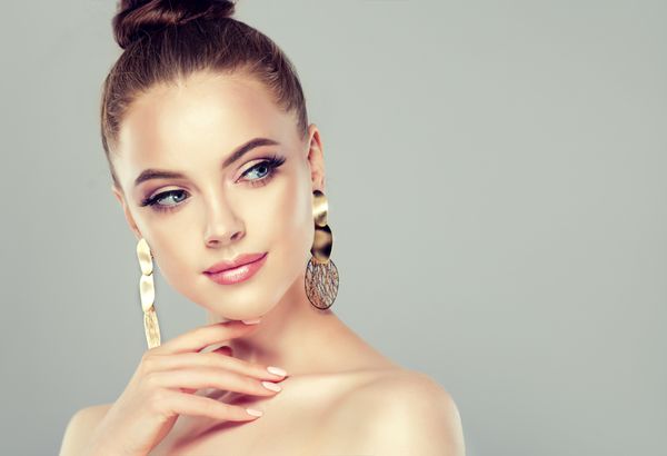 دختر مدل زیبا با مانیکور صورتی روی ناخن ها آرایش و لوازم آرایشی مد جواهرات گوشواره بزرگ و درخشان طلایی