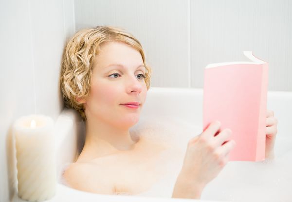 زن جوان مبارک با آرامش و خواندن کتاب در حمام