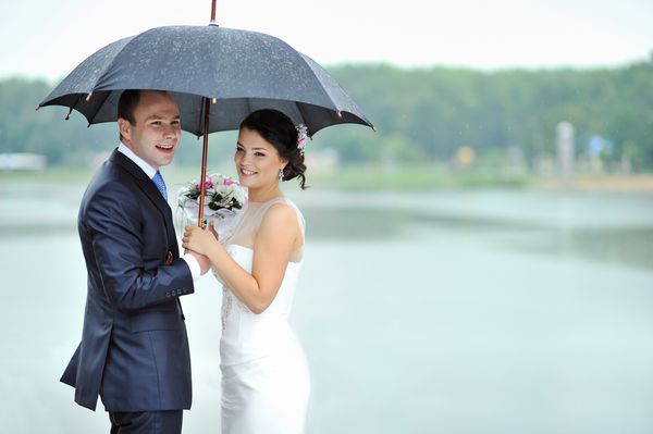 عروس و داماد مبارک در یک روز عروسی بارانی که از باران پنهان شده است