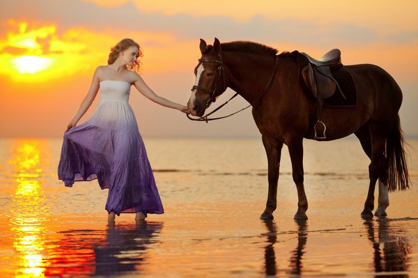 زن زیبا سوار بر اسب در غروب آفتاب در ساحل جیر جوان