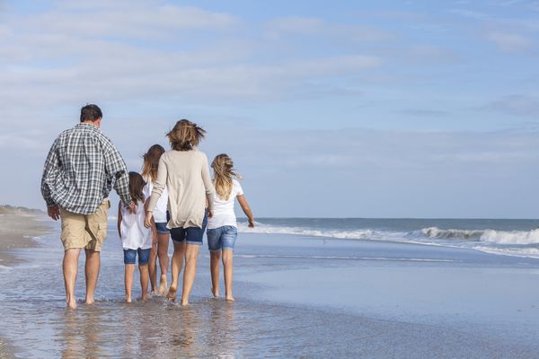 والدین خانواده فرزندان دخترانی که در ساحل قدم می زنند