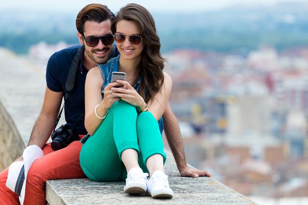 زن و شوهر جوان توریستی در شهر با استفاده از تلفن همراه