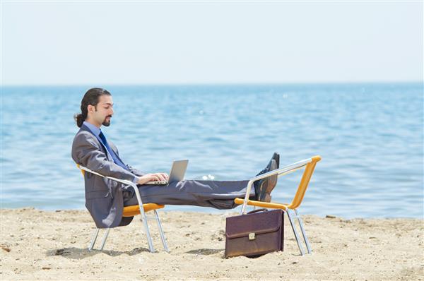 تاجری که روی لپ تاپ در ساحل کار می کند