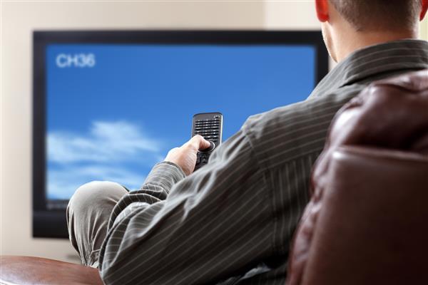مردی که روی مبل نشسته و تلویزیون را در دست دارد و کنترل از راه دور را در دست دارد