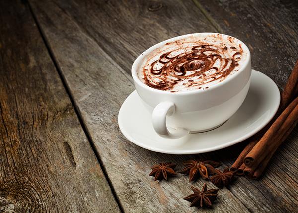 فنجان قهوه و لوبیا چوب دارچین آجیل و شکلات روی میز چوبی روی زمینه قهوه ای
