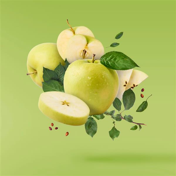 پرواز در هوا سیب و برگ برگ سبز کامل و بریده شده بر روی پس زمینه سبز مفهوم جذب غذا کیفیت بالا