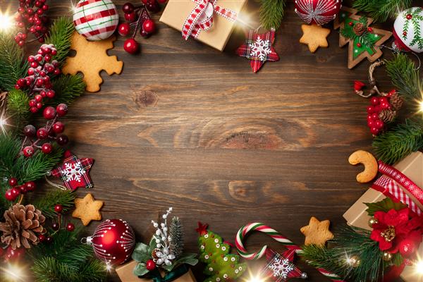قاب با شاخه های صنوبر کلوچه ها و تزئینات کریسمس در زمینه چوبی تیره نمای بالا