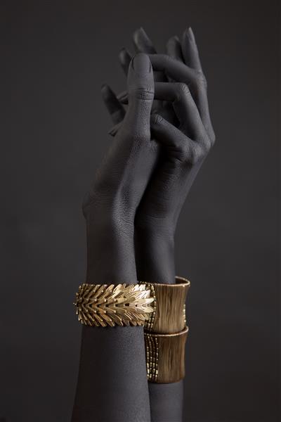 دستهای زن سیاه پوست با جواهرات طلا دستبندهای شرقی روی دست مشکی نقاشی شده جواهرات طلا و لوازم جانبی لوکس در نمای نزدیک زمینه سیاه مفهوم هنر High Fashion