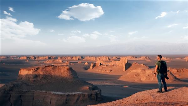 مسافری در پس زمینه سازندهای صخره ای در صحرای دشت لوت طبیعت ایران پرشیا