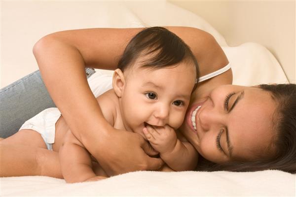 مادر و پسر روی تخت دراز کشیده و مادر در آغوش گرفتن کودک شیرخوار که دست خود را به دهان گذاشته است