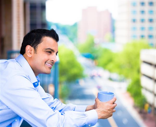 یک پسر خوشحال که از روز خود در حال نوشیدن قهوه جدا شده در پس زمینه شهر لذت می برد