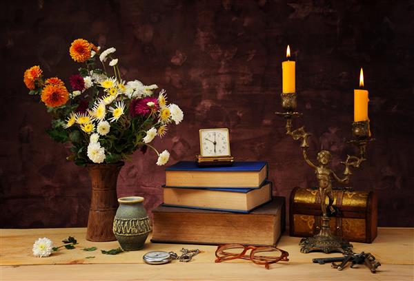 گل در یک گلدان کتاب و شمعدان روی میز
