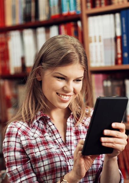 تاجر جوان خندان با تبلت iPad در فروشگاه کتاب یا کتابخانه