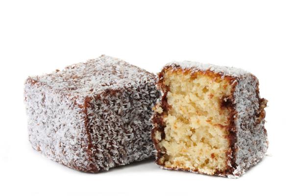 لمینگتون که روی سفید جدا شده است کیک اسفنجی سنتی استرالیایی در شکلات غوطه ور شد سپس در نارگیل غلت خورد