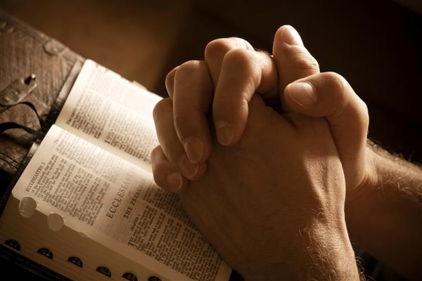 دستها در نماز بسته بر روی کتاب مقدس باز