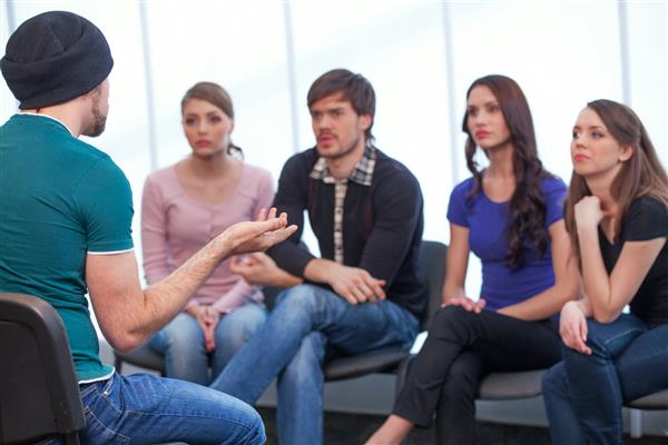 مرد جوان سمینار برگزار می کند چهار نفر در حال نشستن به یک مرد گوش می دهند
