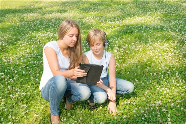 دختر و پسر در پارک نشسته اند و از یک تبلت دیجیتال لذت می برند