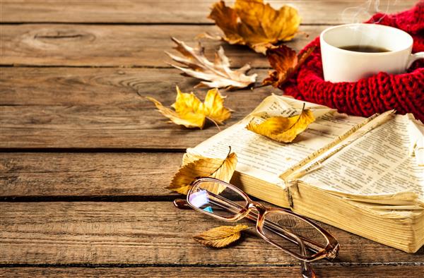 قهوه داغ کتاب جذاب لیوان ها و برگ های پاییزی در زمینه چوب - مفهوم استراحت یا بازنشستگی با فضای نوشتاری آزاد