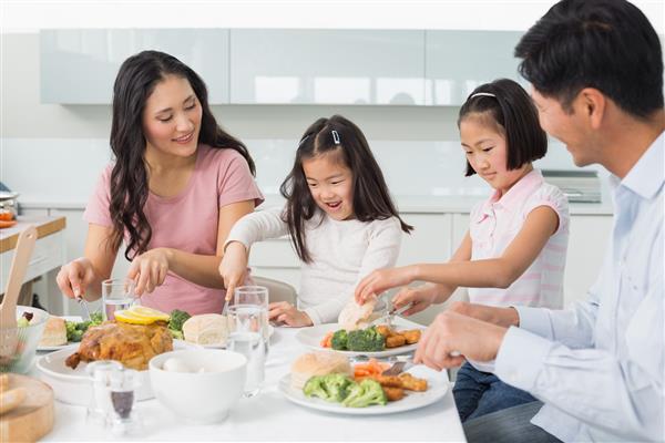 یک خانواده چهار نفره خوشحال که از غذای سالم در آشپزخانه در خانه لذت می برند