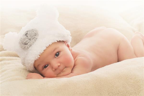پرتره پسر بچه تازه متولد شده بیدار که کلاه خرس شکل خنده دار روی پوشش بژ نرم دارد