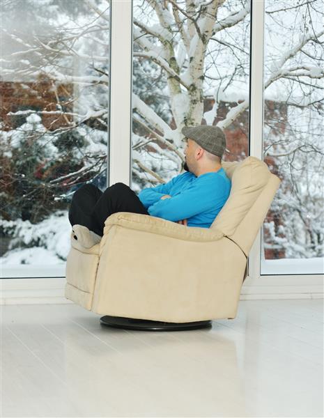 مرد جوان در زمان برف زمستانی روی مبل سفید در خانه در حال استراحت است