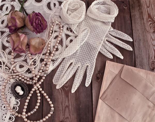 جواهرات و دستکش های زنانه قدیمی مفهومی برش خورده با گلهای رز خشک در زمینه چوبی