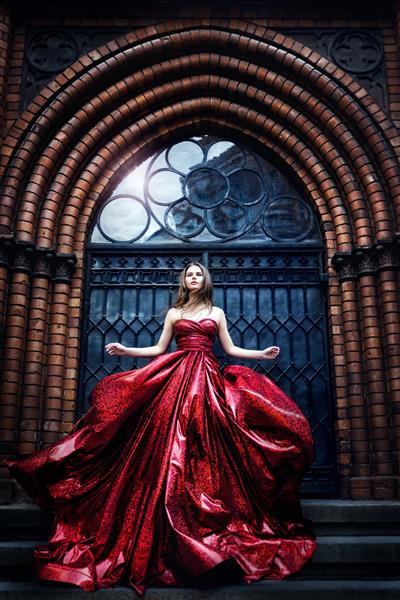 مدل مد در نزدیکی درب دروازه قلعه قرون وسطایی پرتره زرق و برق زن زیبایی در لباس قرمز تکان دهنده زیبا