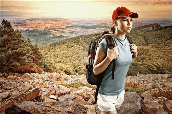 کوهنورد زن جوانی کلاه پوشیده و کوله پشتی را در کوه و تپه ها پیاده روی کرده است مسافر زن راضی در نوردی لباس ورزشی هنگام غروب آفتاب