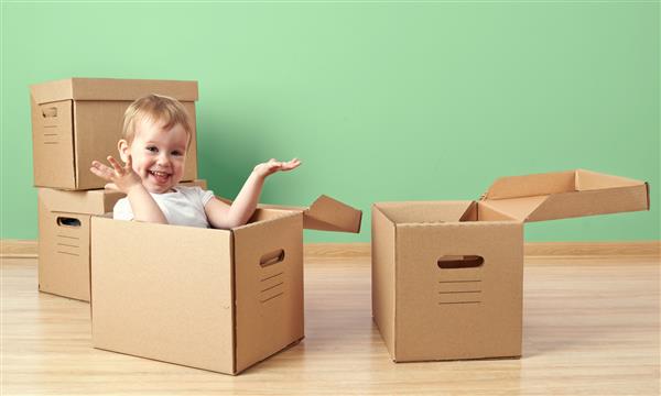 کودک نوپای کودک که در یک اتاق خالی در جعبه مقوا نشسته است